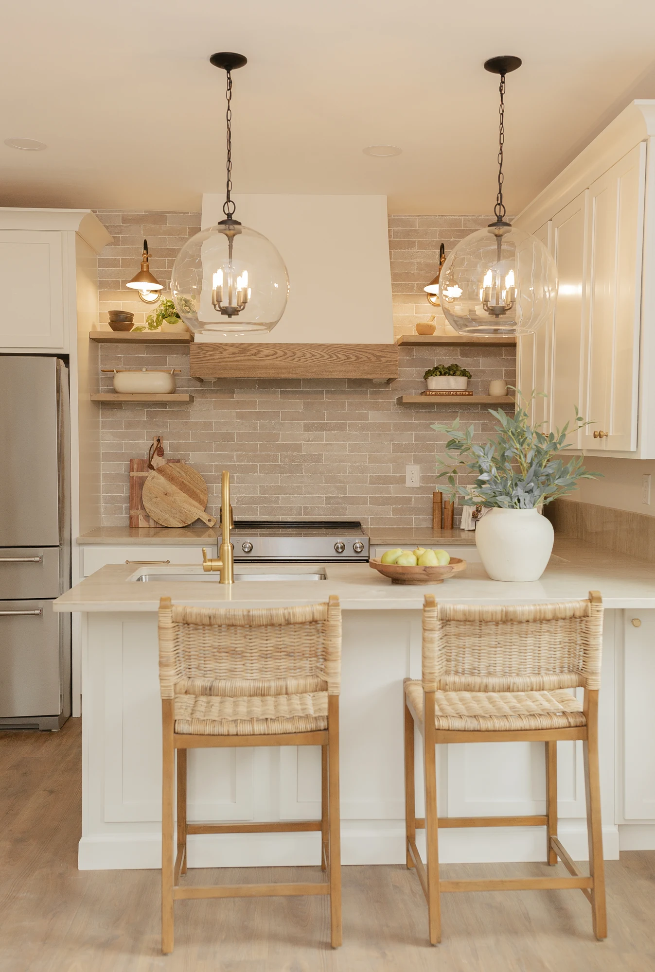 Tolland Stage kitchen with glass pendants, warm wood shelves and woven chairs.
